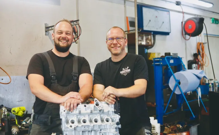 Zwei Mitarbeiter mit einem aufbereiteten Motorblock in der Werkstatt