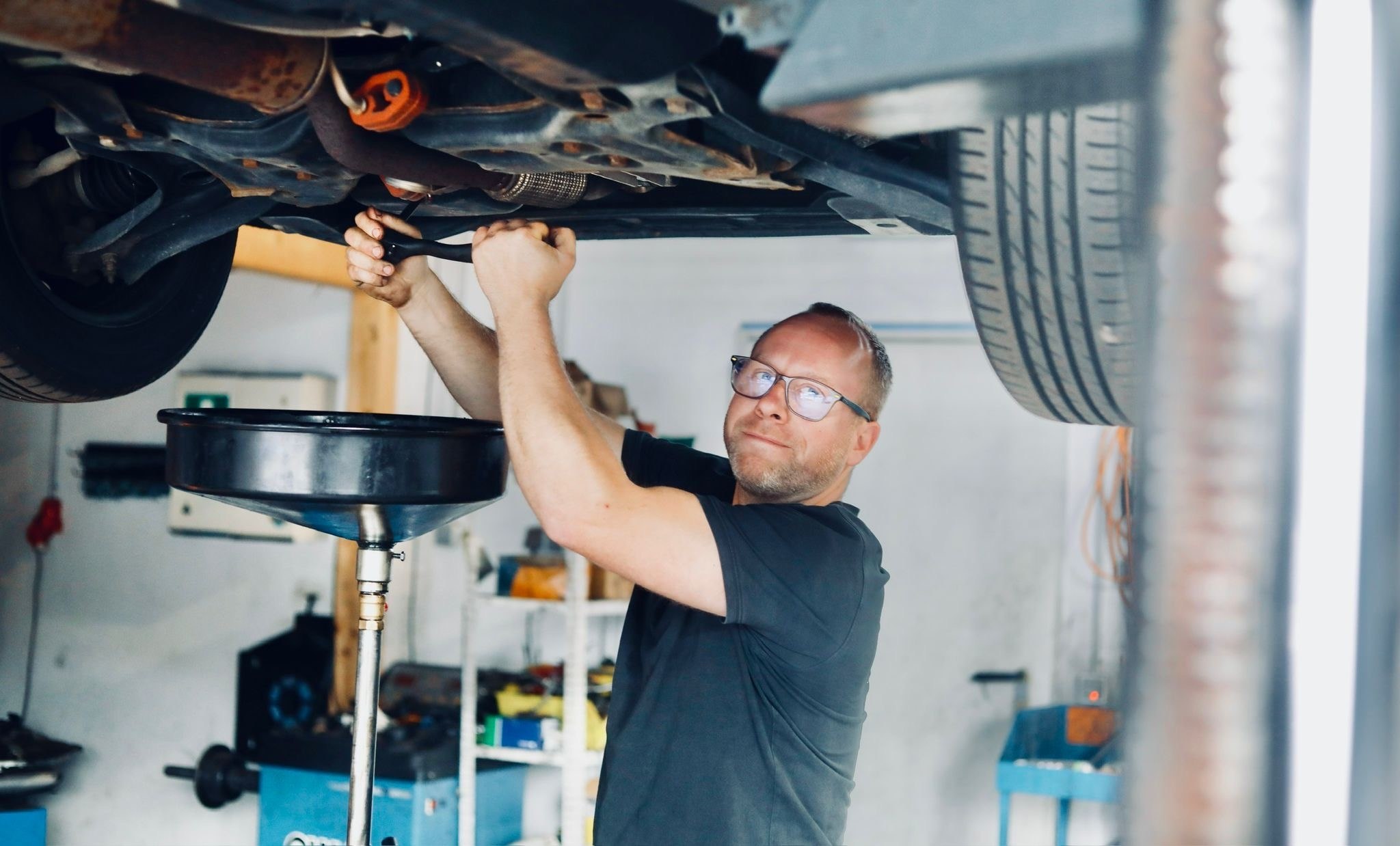 KFZ-Meister bei der Arbeit unter einem Fahrzeug auf der Hebebühne
